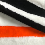 Detail of a minimalist striped rug in black and white sheepskin, with an orange accent stripe. 